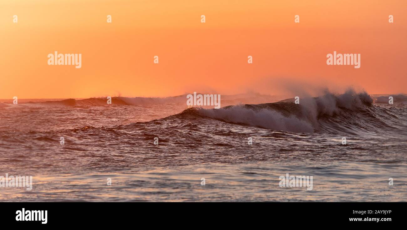 waves breaking at sunset creating spray Stock Photo