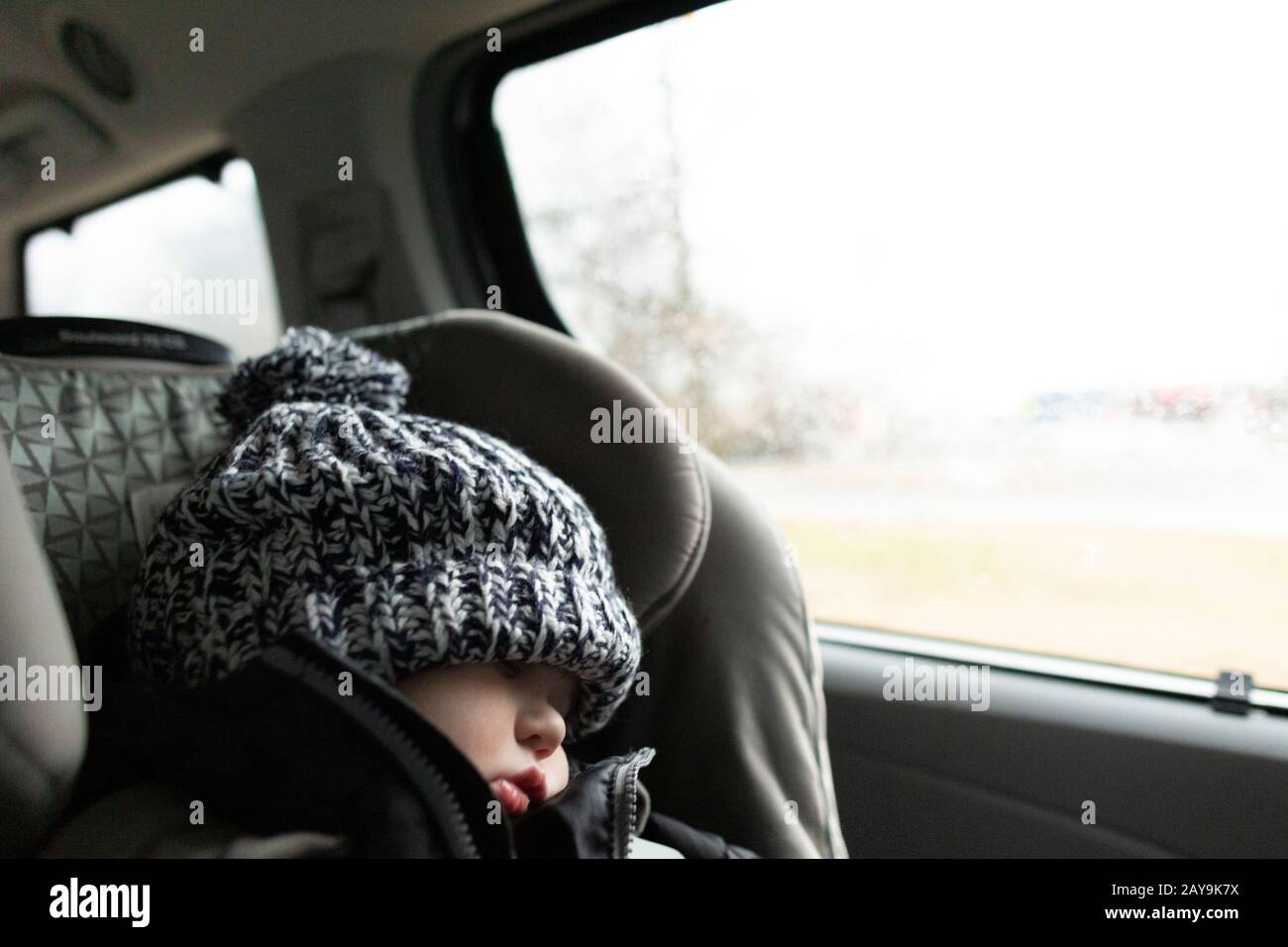 Toddler wearing winter hat sleeps while in carseat inside minivan Stock Photo