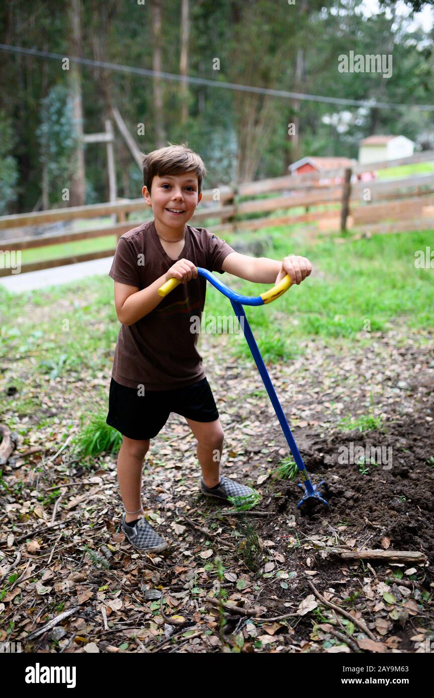 Boy smiling in the yard while he tills soil for a garden Stock Photo