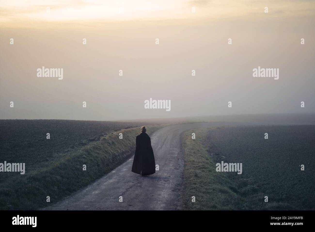 woman with long coat walks in a path in a fog Stock Photo