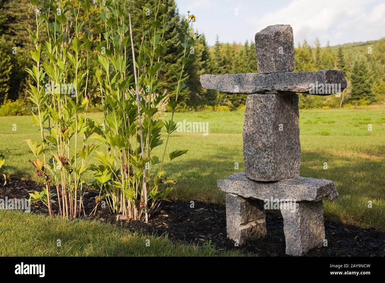 Stacked granite Inukshuk rock sculpture in black mulch border in backyard country garden in summer. Stock Photo