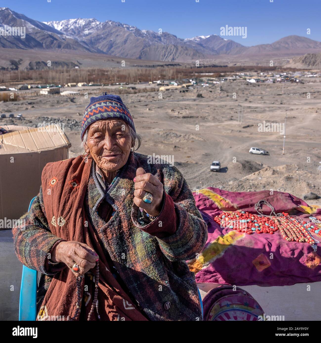 Ladakh woman selling beads, Ladakh range in background, Spituk Gompa, Leh, Ladakh Stock Photo