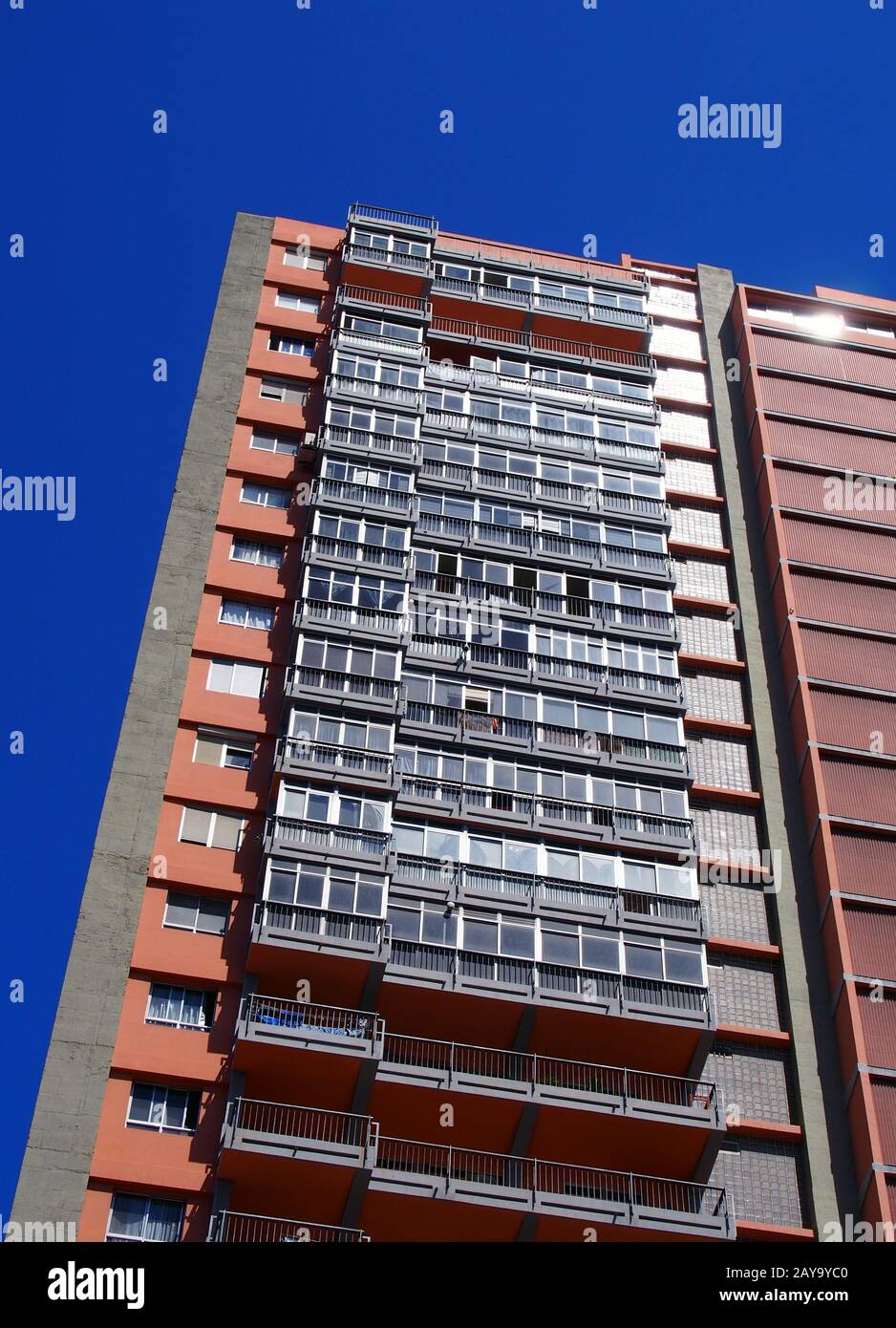 vertical angled view of a tall concrete apartment block with balconies against a blue sky Stock Photo