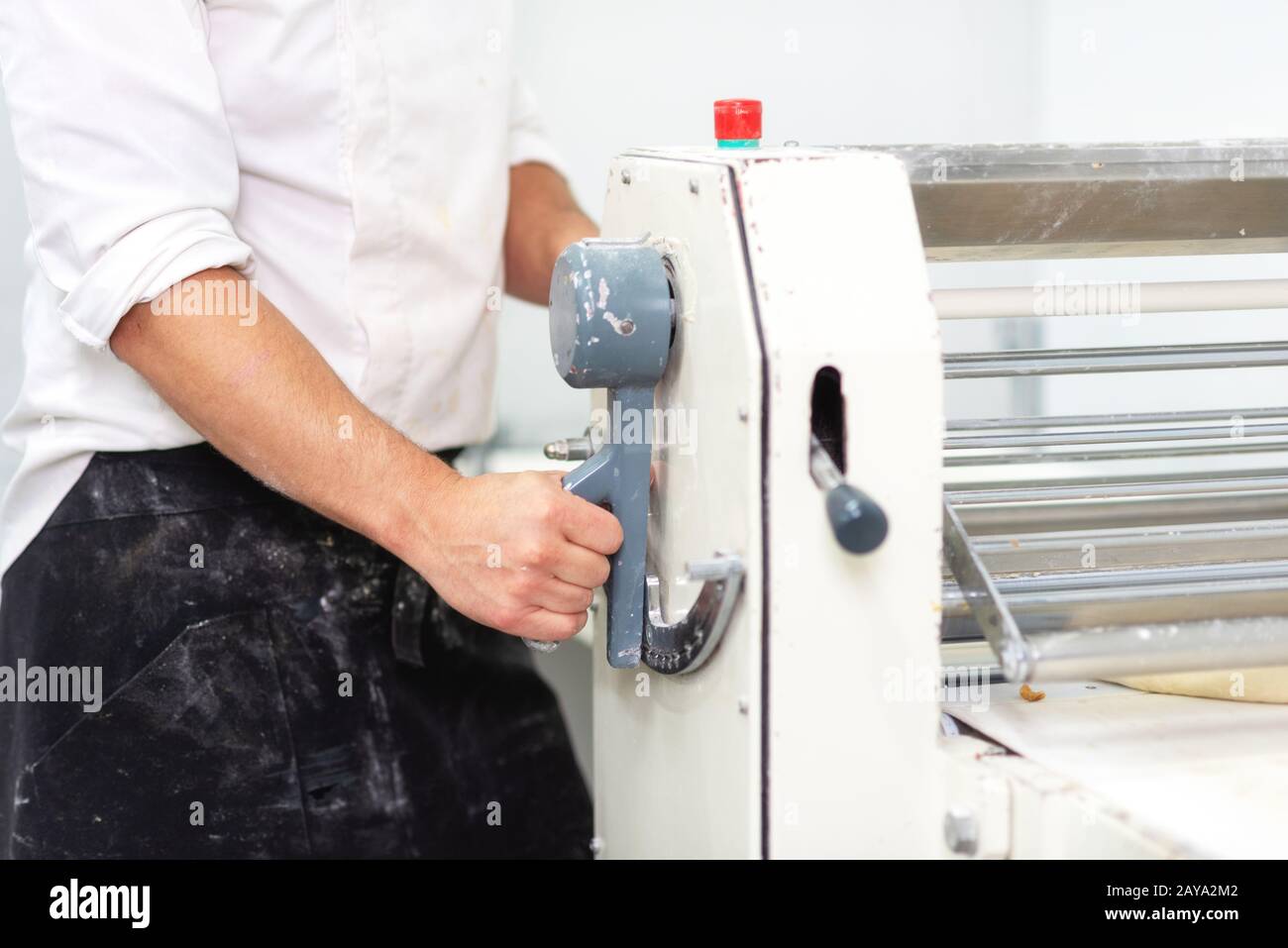 Baker using dough sheeter machine to produce croissants dough at the