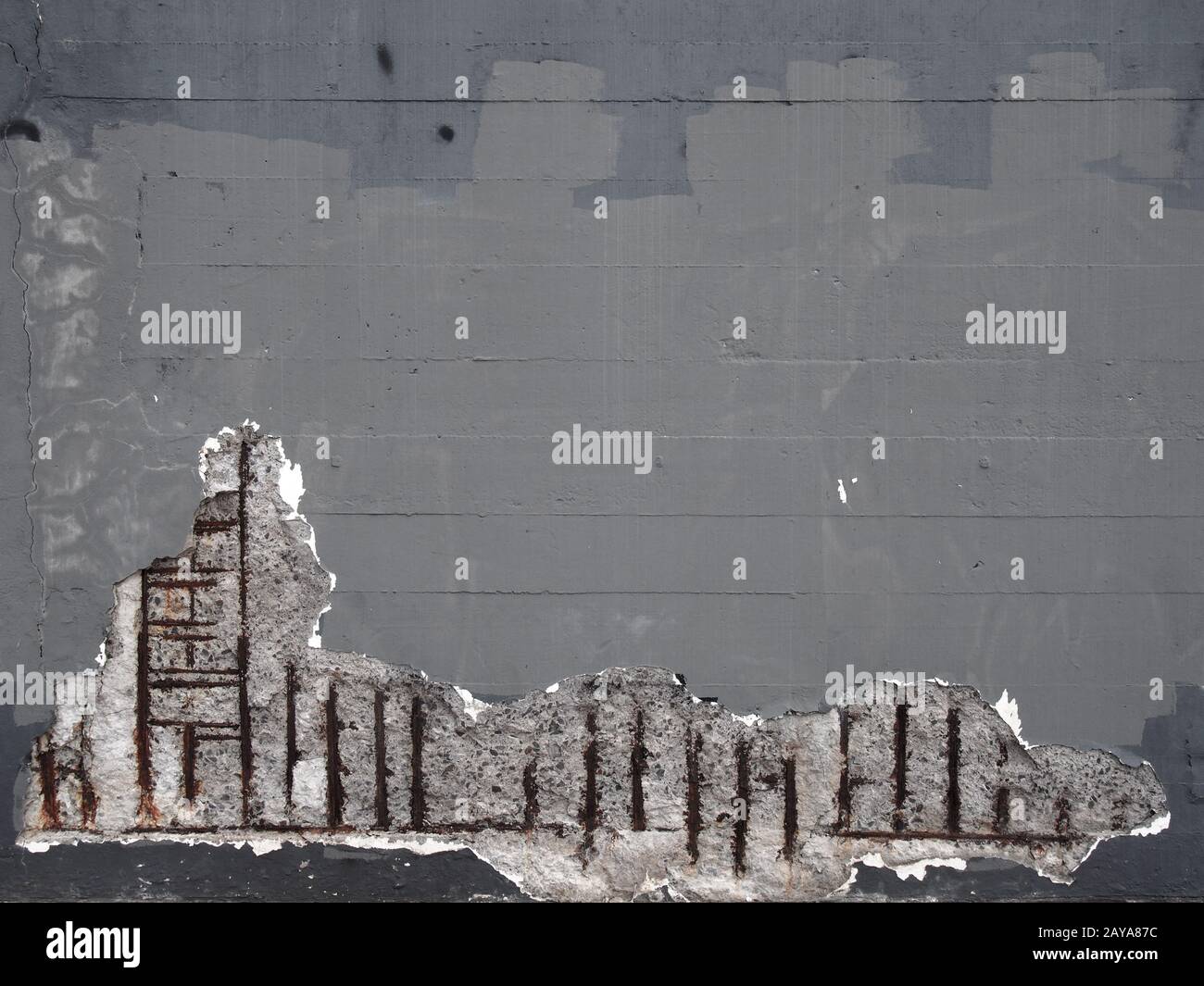 an old grey painted concrete wall with corroding rusty steel reinforcement bars causing damage to the structure Stock Photo