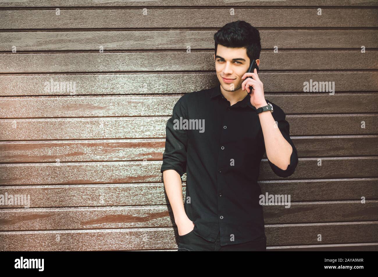 Portrait model young handsome male suspect Turkish middle eastern brunette in black shirt uses hand phone to call technology on Stock Photo