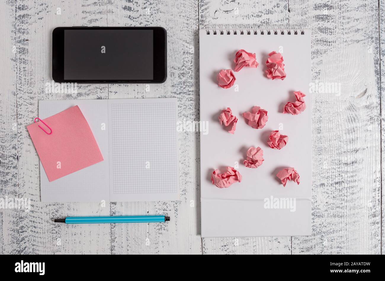 Squared open spiral notebook marker sticky note clip smartphone paper balls lying wooden retro vintage rustic old background. Em Stock Photo
