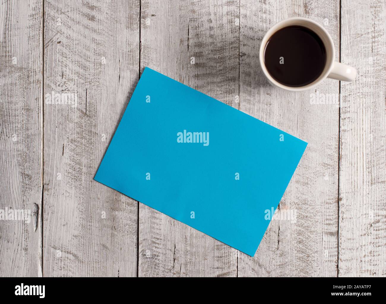 Pastel Colour plain sheet with a cup of black coffee on the wooden background. Empty paper placed next to mug drink above table. Stock Photo