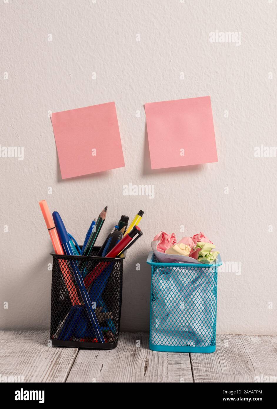 Workplace with Two Empty Pink Stick Pad Notes Put on White Wall Hanging above Two Full Pencil Pots on Work Desk Filled with Pens Stock Photo