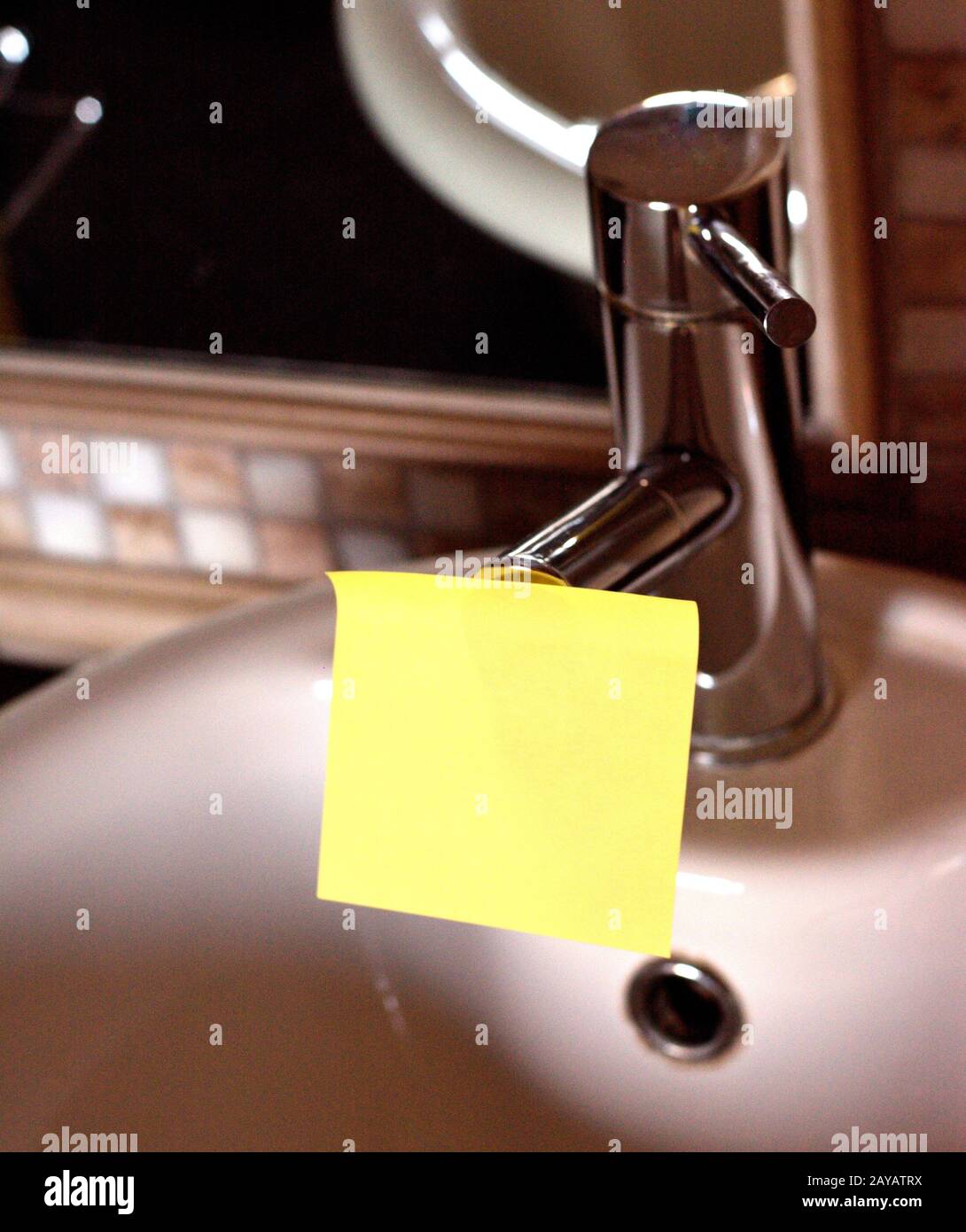 Rectangular yellow note paper attached on toilet sink faucet. Piece of square sheet use to give notation stick to water tap in t Stock Photo