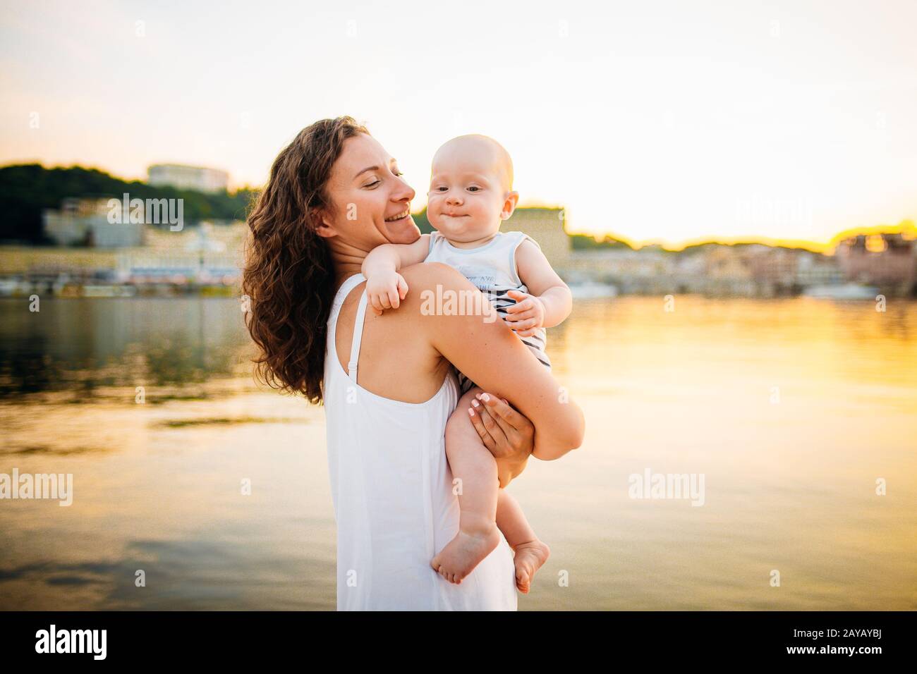 Happy family on the beach. Son child mother boy and baby hugging on beach near river or lake. Happy family on the beach. Mom and Stock Photo