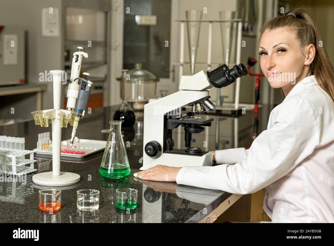 Young female laboratory technician sitting next to compound microscope Stock Photo