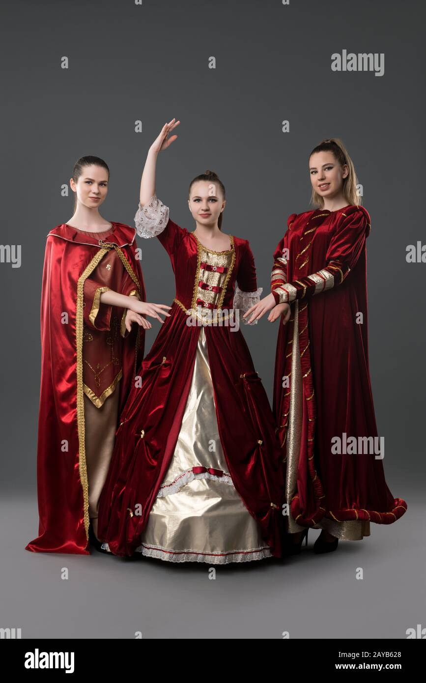 Three girls in gorgeous queen red dresses view Stock Photo