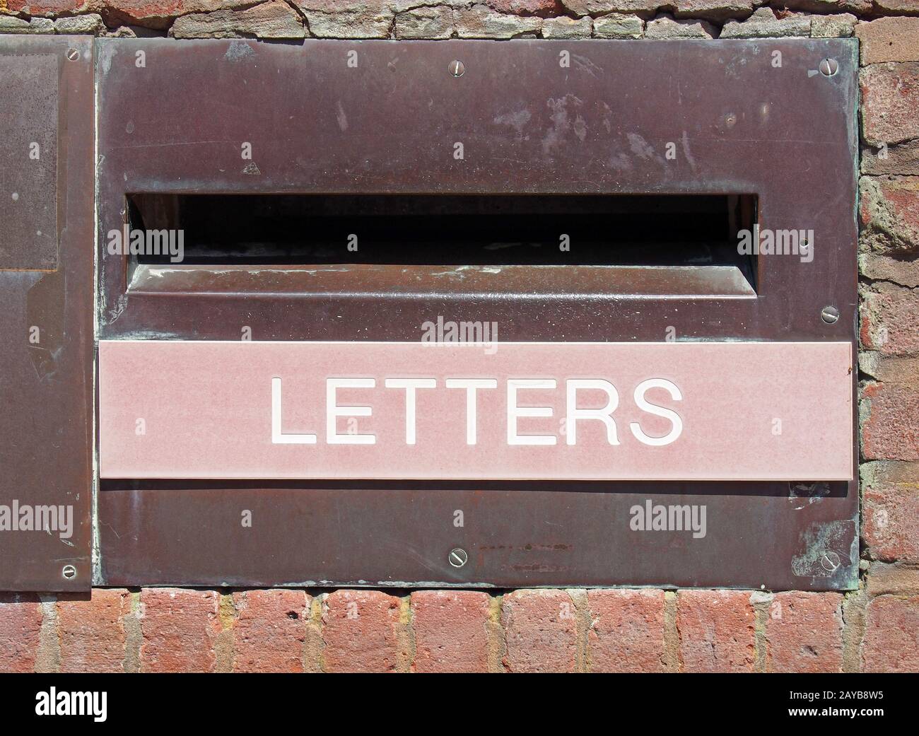 old british postal mail box in a brick wall with rusted metal surround and the word letters on a faded red panel Stock Photo