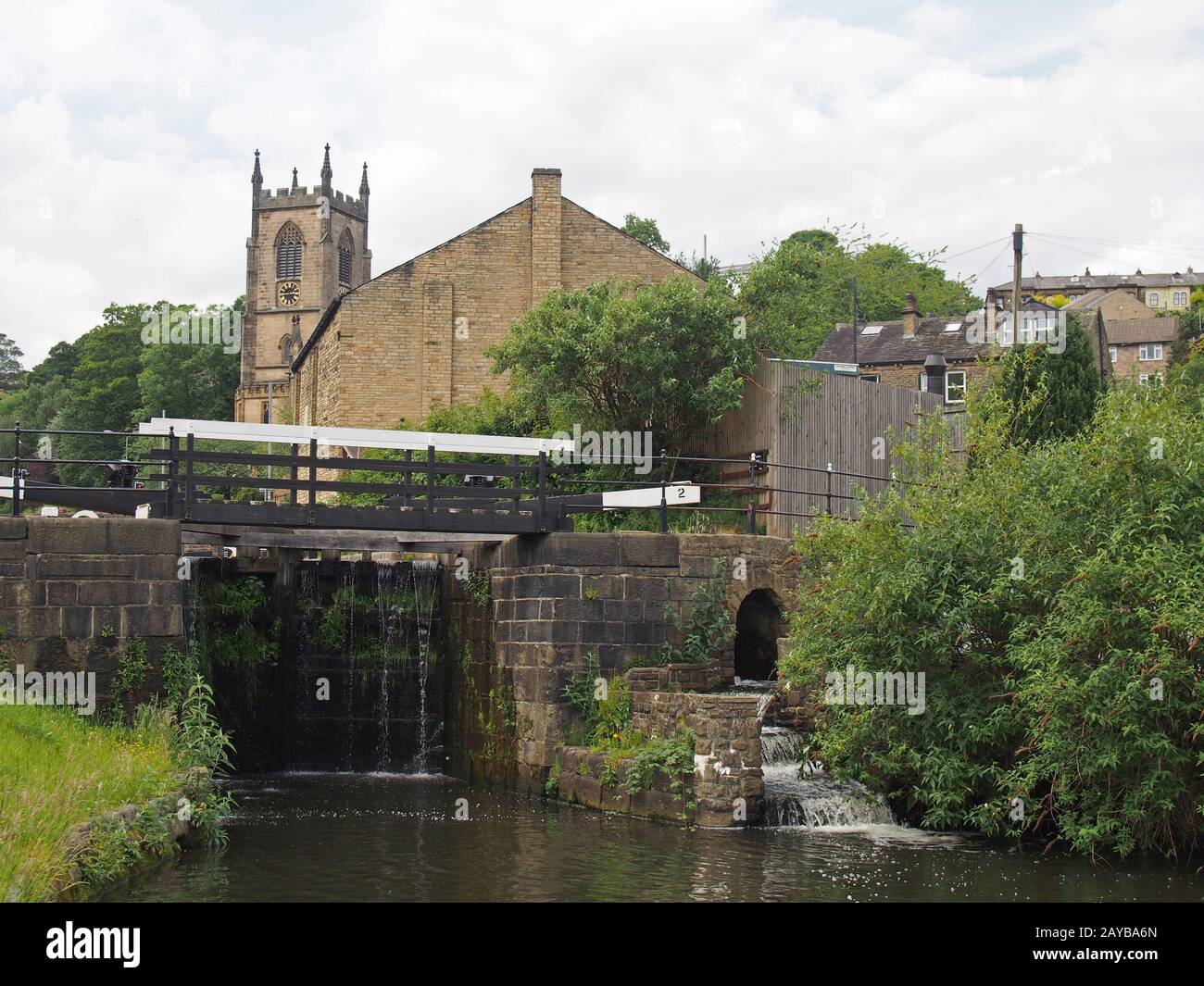 lock gates on the canal in sowerby bridge in west yorkshire with the historic christ church building surrounded by trees Stock Photo