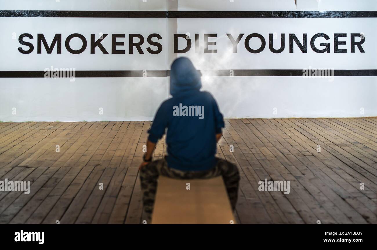 Teenager smoking and message on wall Smokers die younger. No smoking