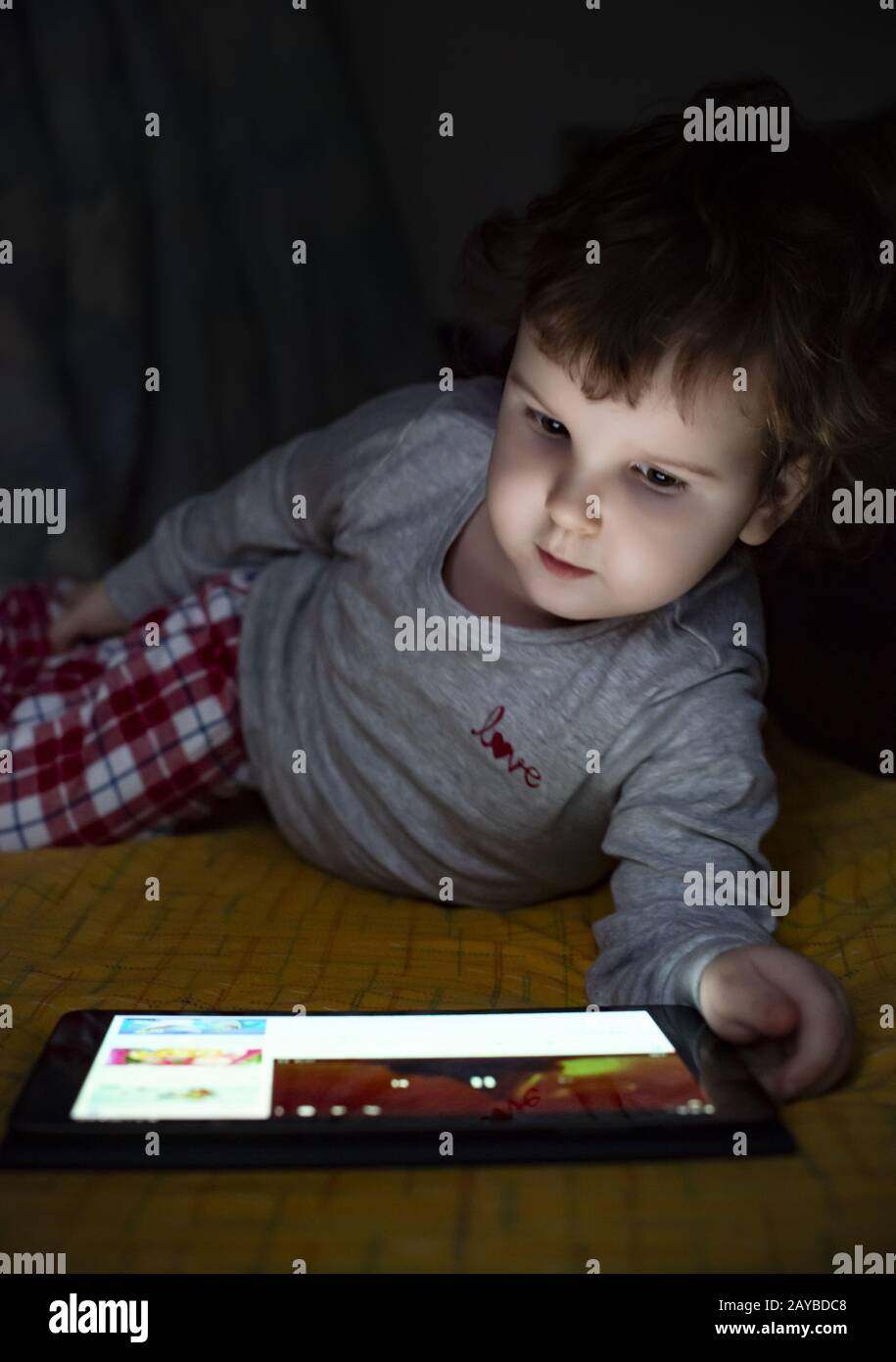 Little girl watching her tablet in the bed. Illuminated child face from