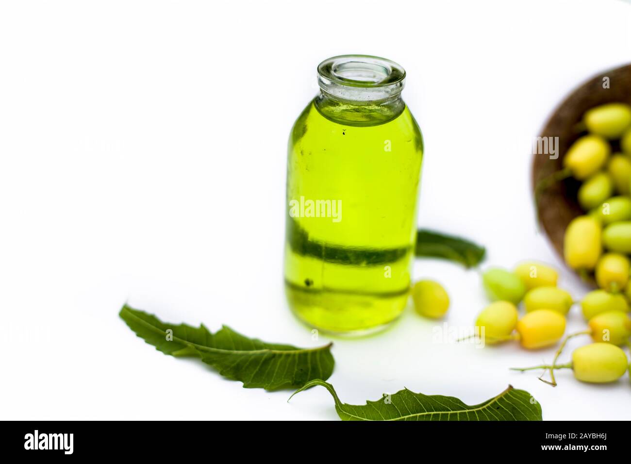 Fresh green neem fruit of Indian Lilac fruit in a clay bowl isolated on white along with its oil in a transparent glass bottle.Horizontal shot. Stock Photo