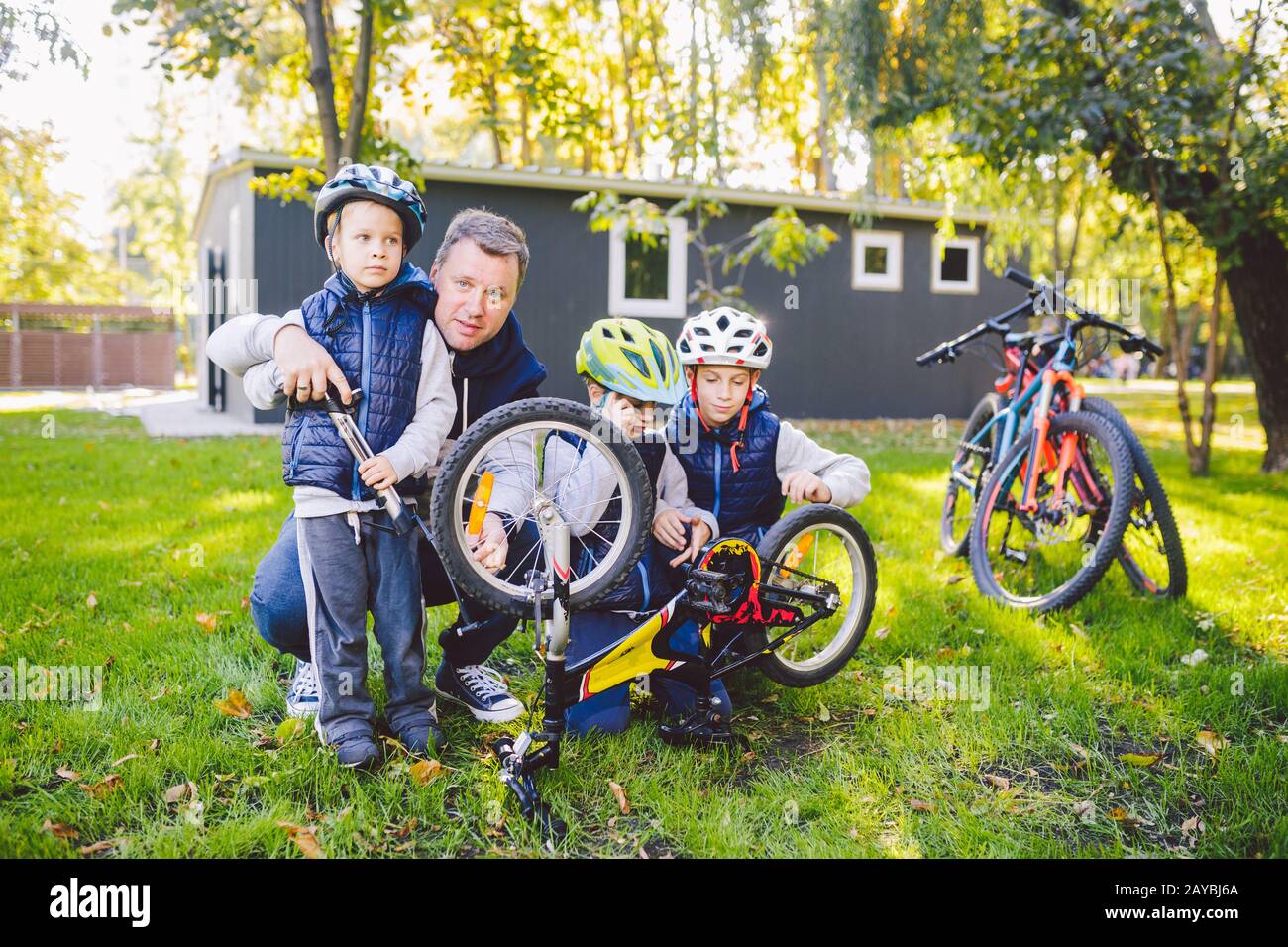Father's day A big friendly family father and three sons joint active rest outside. Dad teaches sons to repair cycling. The chil Stock Photo
