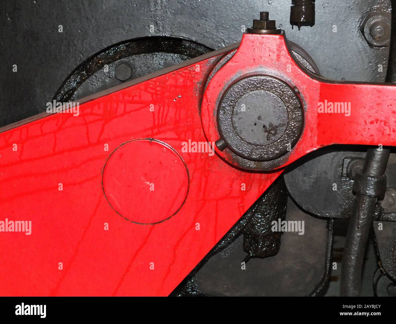 details of black steam locomotive wheel with red drive and connecting rods with bolts and leaking oil Stock Photo