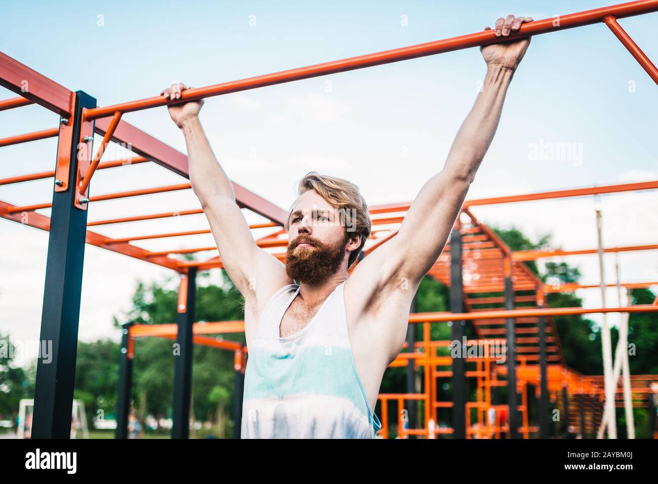 strong athlete doing pull-up on horizontal bar. Muscular man doing pull ups on horizontal bar in park. Gymnastic Bar During Work Stock Photo