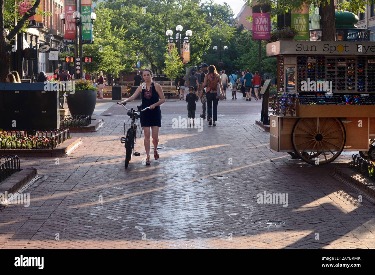 A woman walks her bike on Pearl Street Mall in Boulder, CO. Bike riding is not allowed on the mall. Stock Photo