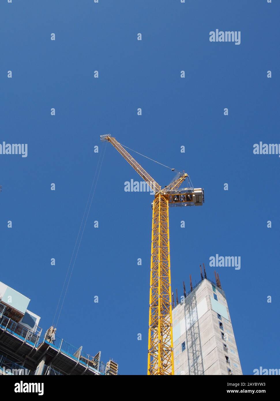 a view of a tall tower crane working on large construction sites against a blue sky Stock Photo
