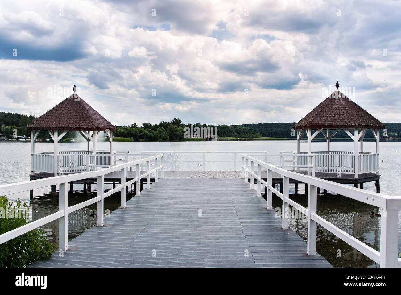 White roofed pier with wooden huts on lake, green forest and clouds in background, Poland Stock Photo