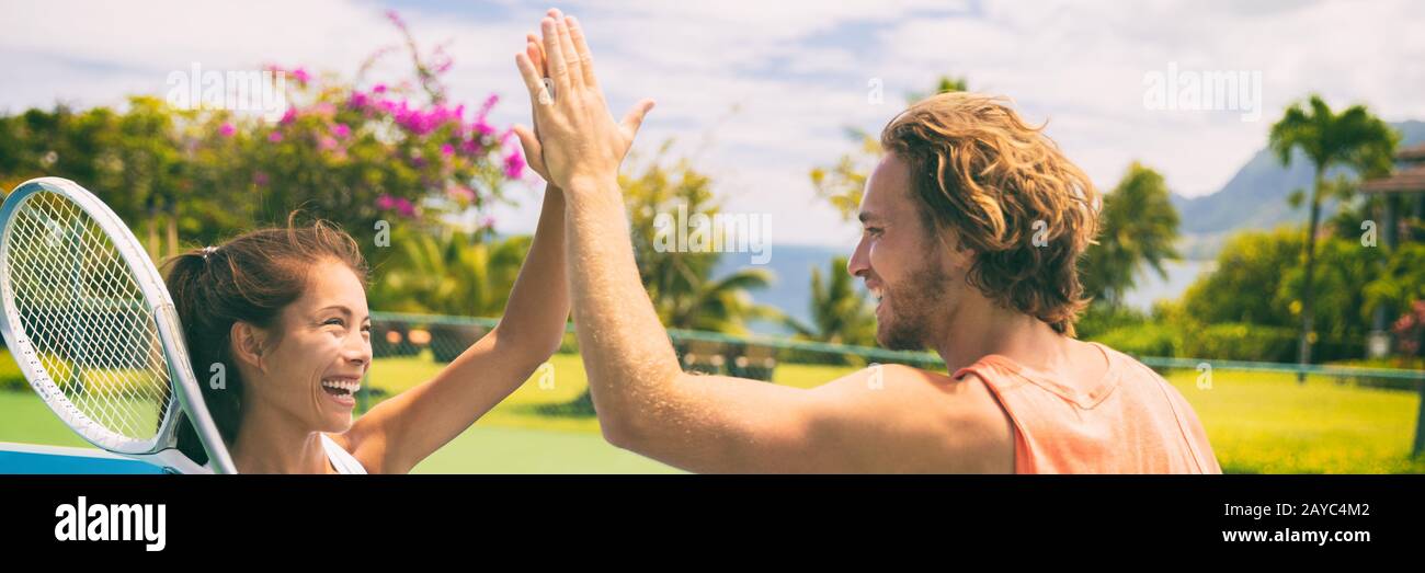 Summer sport tennis players having fun doing high five after game. Healthy lifestyle outdoor living mixed doubles banner panorama. Stock Photo