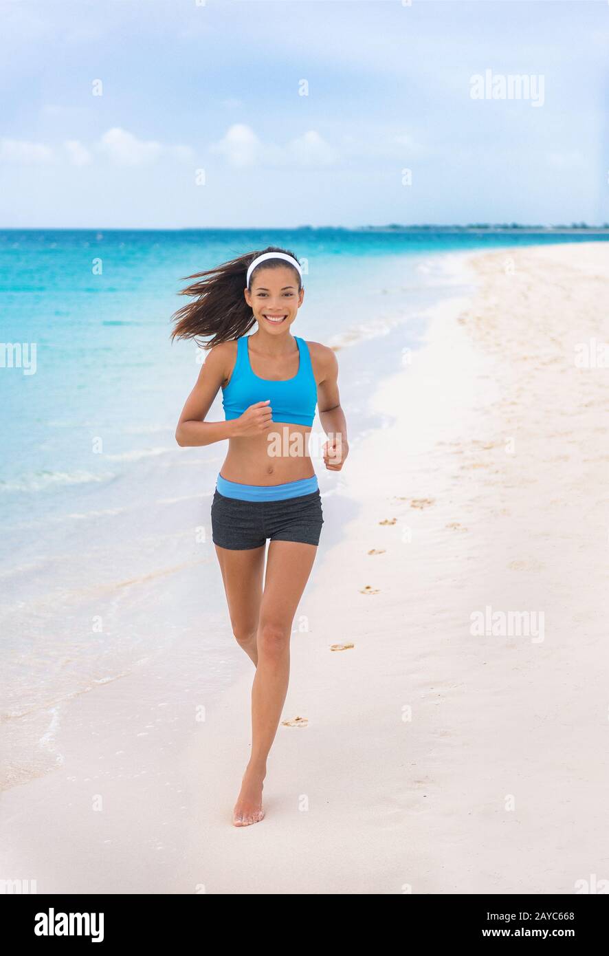 Running on beach fitness runner sportswear woman. happy Asian fit girl  training jogging in blue sports bra and shorts on summer tropical vacation  destination. Healthy active lifestyle on travel Stock Photo -