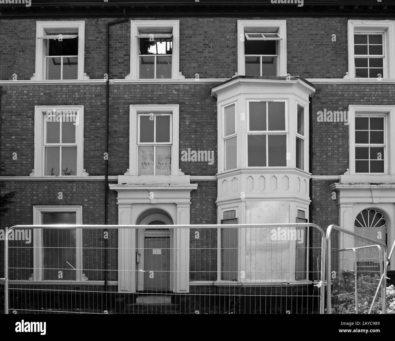 monochrome image of a row of abandoned dilapidated derelict houses in a street behind a metal fence in southport merseyside Stock Photo