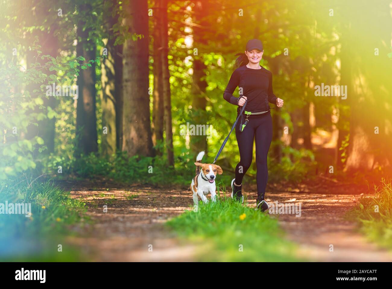 Girl is running with a dog (Beagle) on a leash in the spring time, sunny day in forest Stock Photo