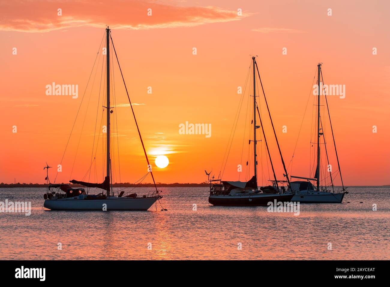 Three sailboats on sea at sunset Stock Photo