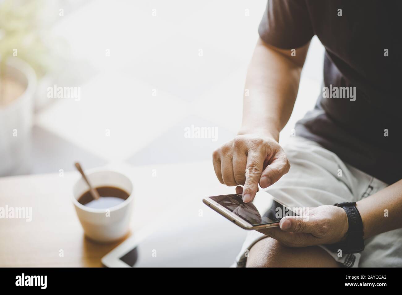 Smartphone in young man hand with digital tablet and coffee . Stock Photo
