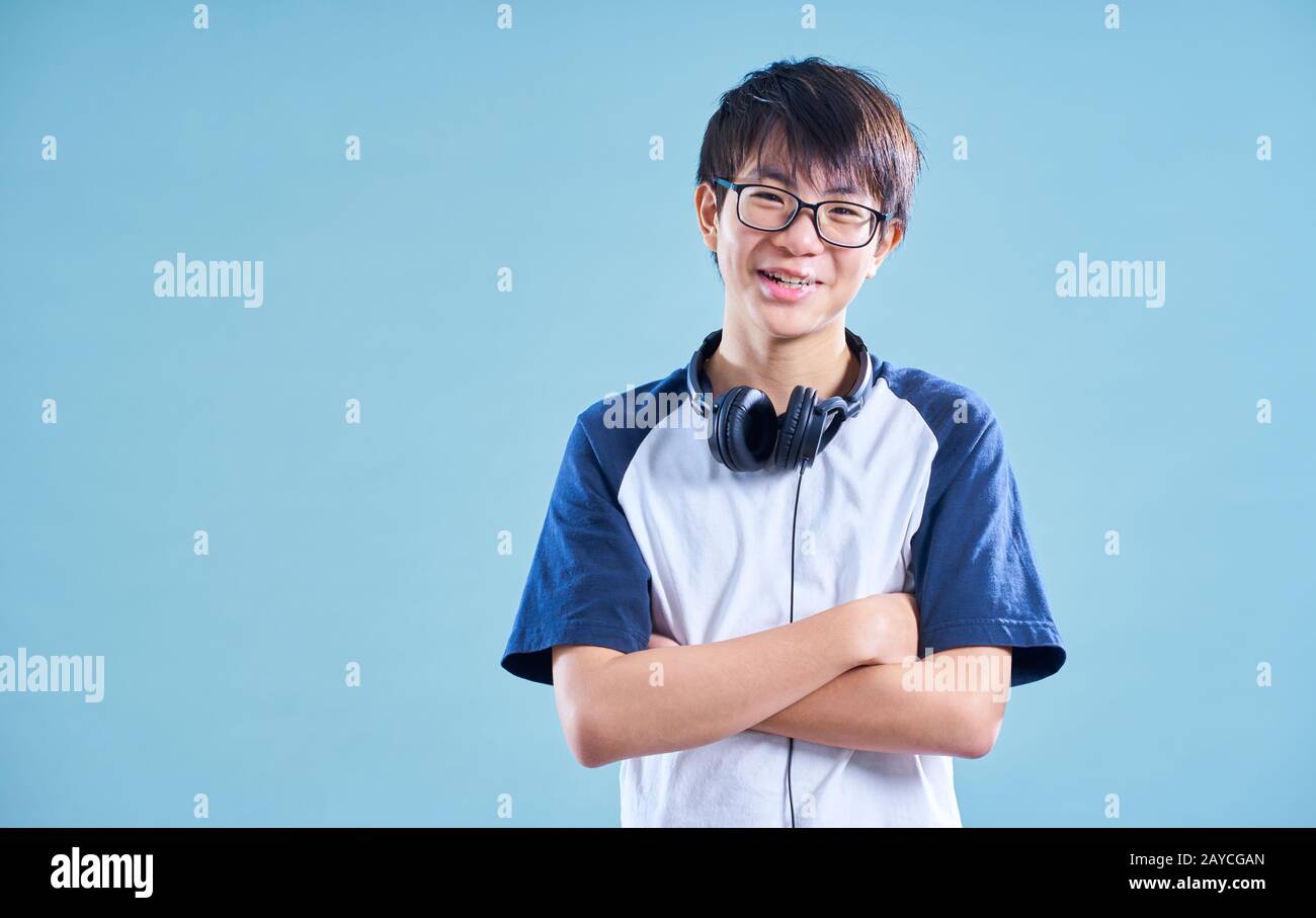 Portrait of Asian teenage smiling boy in studio with light blue background . Music headphone concept . Stock Photo