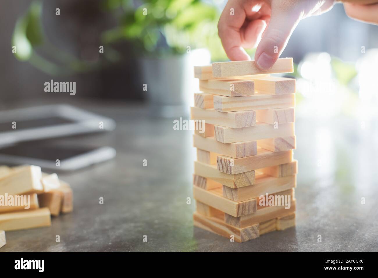 Hand of kid playing a blocks wood tower game of architectural project with sun flare and blur background .Selected focusing . Stock Photo