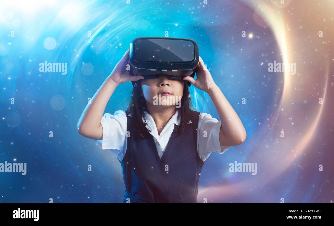 Little asian cute girl wearing virtual reality goggles with amazing cosmic futuristic space virtual imaging background . Stock Photo