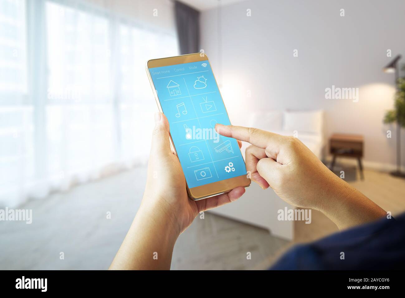 Smart remote home control system apps on a hand phone with blur house  interior background . Stock Photo