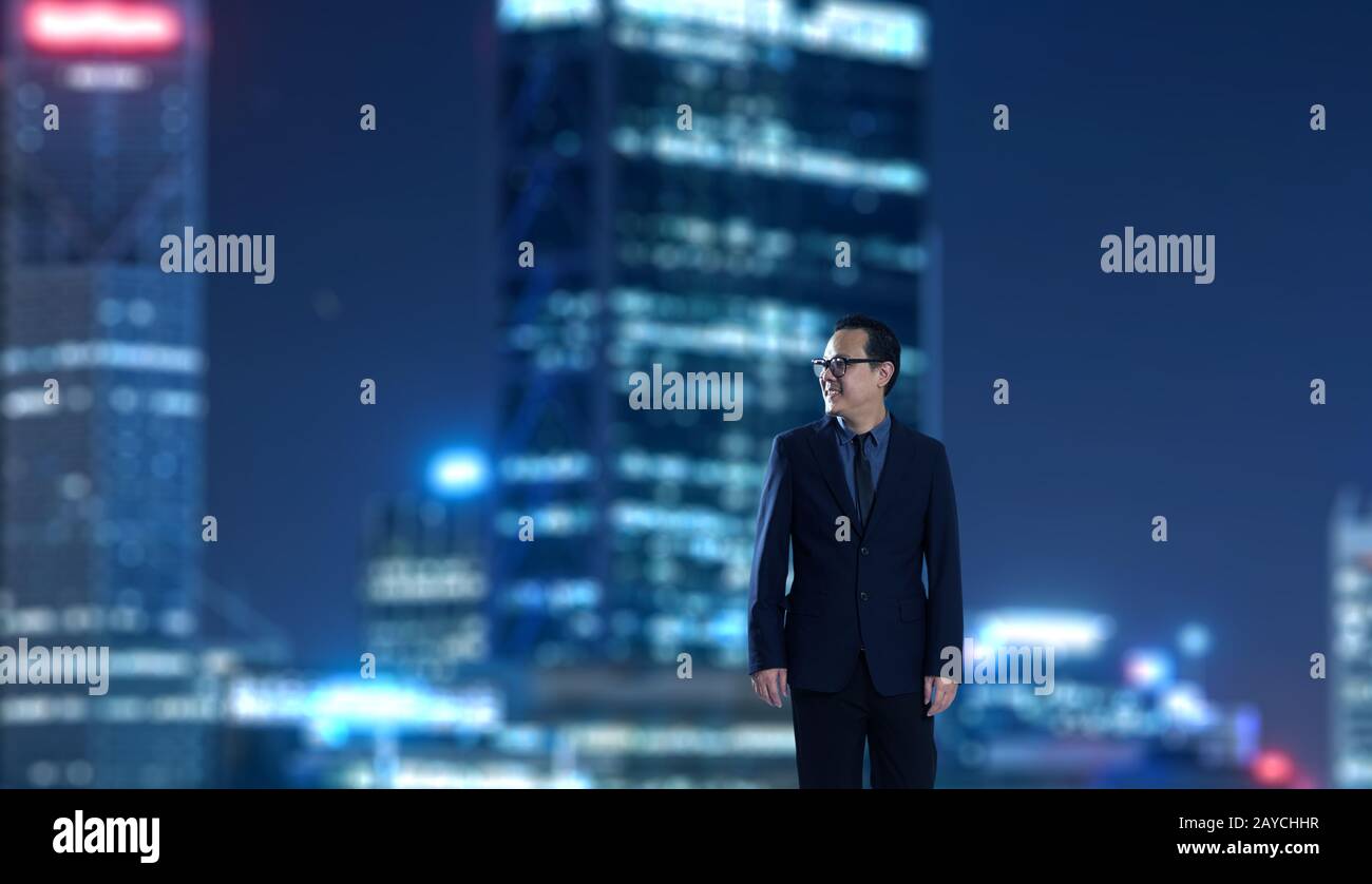 Young businessman standing with out of focus city skyscraper background . Night scene. Stock Photo