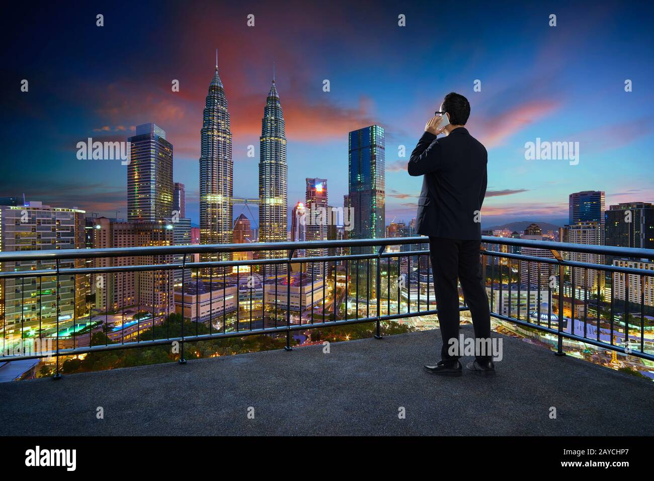 Young businessman standing on a balcony using smartphone with beautiful city  skyline background . Night scene Stock Photo - Alamy