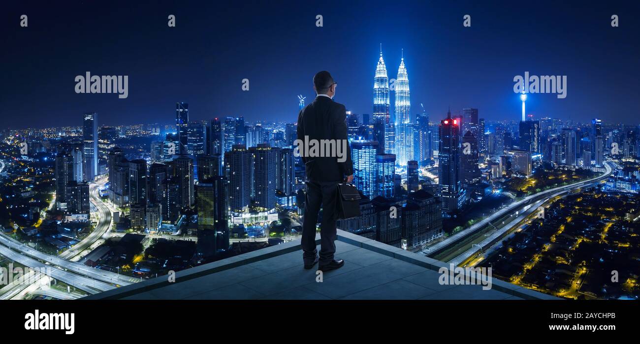 Businessman stand at rooftop looking great cityscape view and thinking business plan of the future . Night scene . Stock Photo