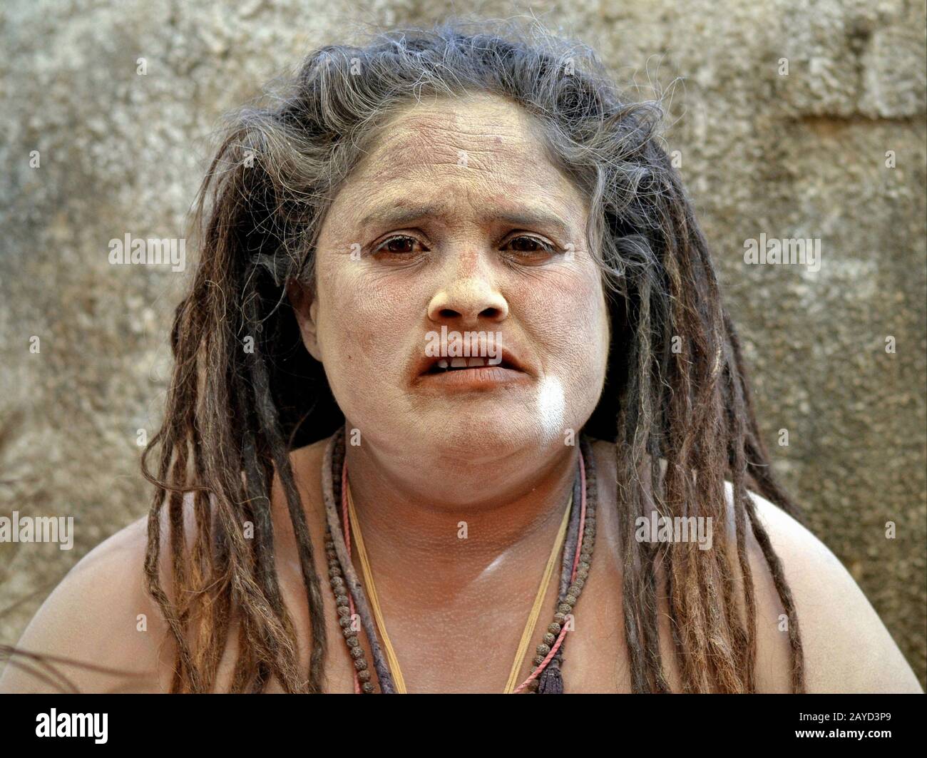 Chubby Indian Hindu female sadhu (sadhvi) with long dreadlocks and sacred ash (vibhuti) on her face and shoulders poses for the camera. Stock Photo