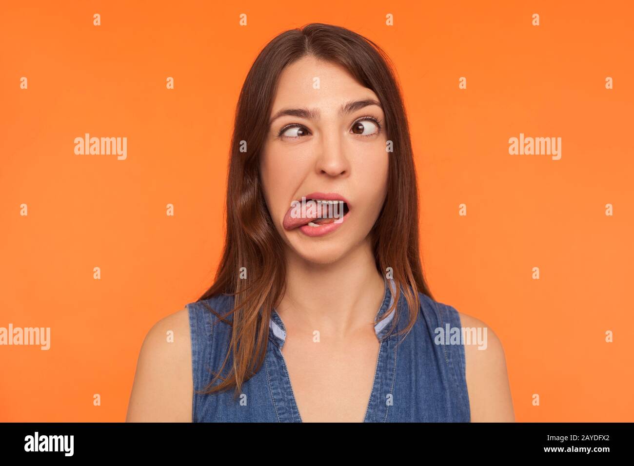 Closeup of silly dumb brunette woman demonstrating tongue and making stupid face with crossed eyes, idiotic expression, showing ridiculous grimace. in Stock Photo