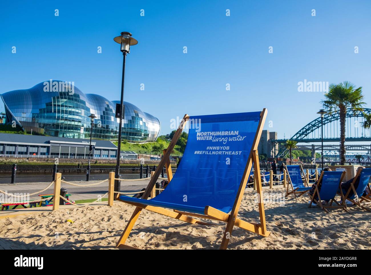 Artificial beach setting with sand and beach chairs on a beautiful summer afternoon at Newcastle Quayside with Sage Gateshead an Stock Photo