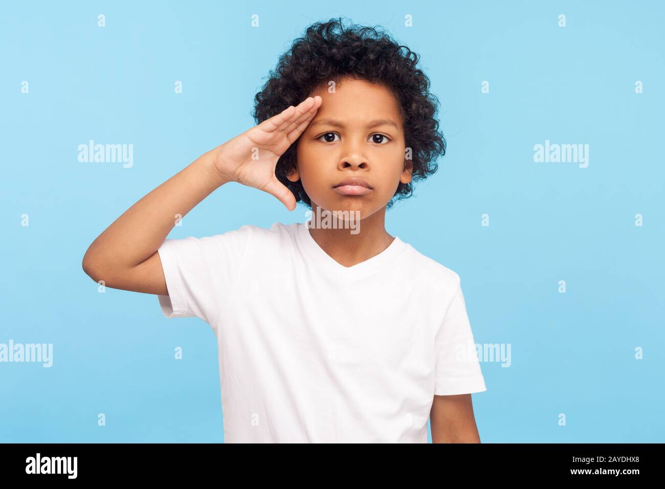 Yes, sir! Portrait of serious little boy with curly hair giving salute