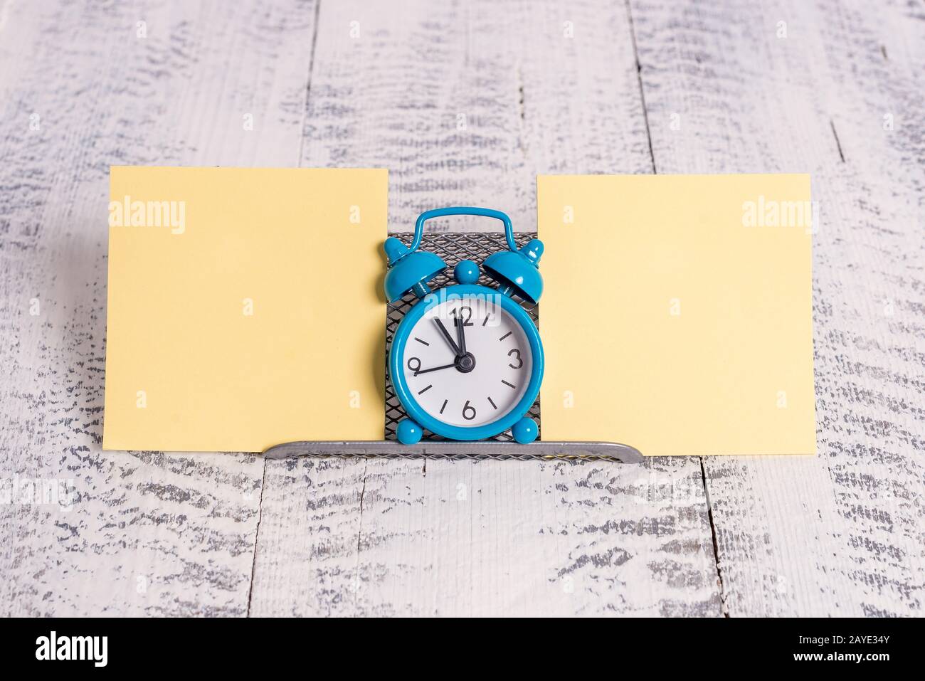 Mini blue colour alarm clock to show time placed in between two yellow notepapers. Classic little watch standing above a buffer Stock Photo