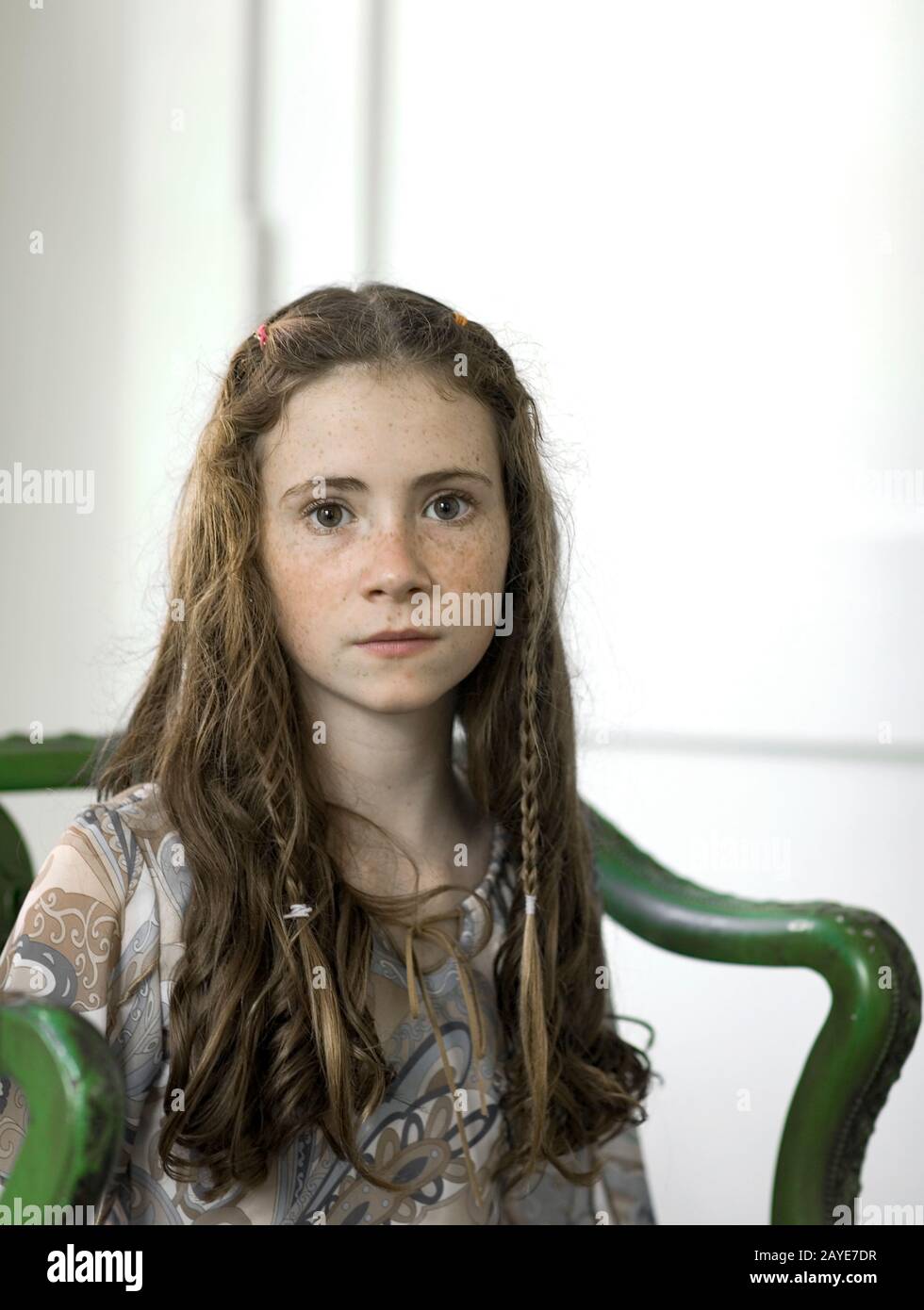 A pretty young girl with freckles and pigtails sitting in an antique green armchair. Stock Photo