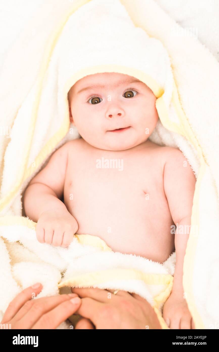 Adorable 6 months old Baby girl infant on a bed on her belly with head up looking into camera with her big eyes. Natural light. Stock Photo