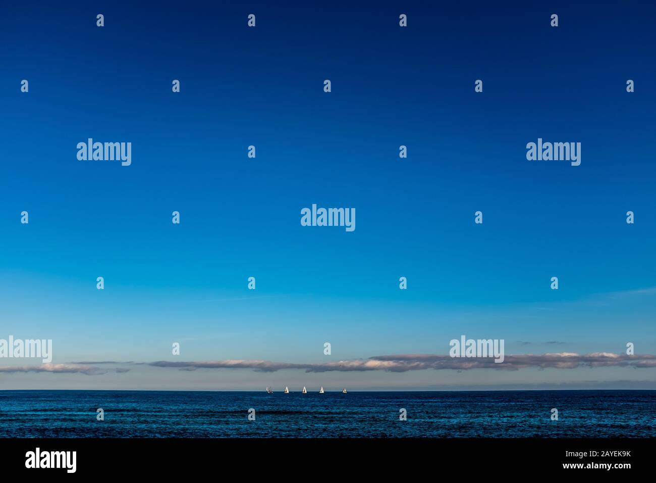 Sailboats on the horizon line on the sea, looking at view from the beach of Barcelona (Spain) on a lukewarm winter afternoon. Different shades of blue. Stock Photo