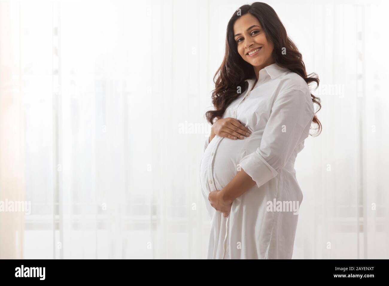 Pregnant woman smiling while holding her belly bump Stock Photo - Alamy